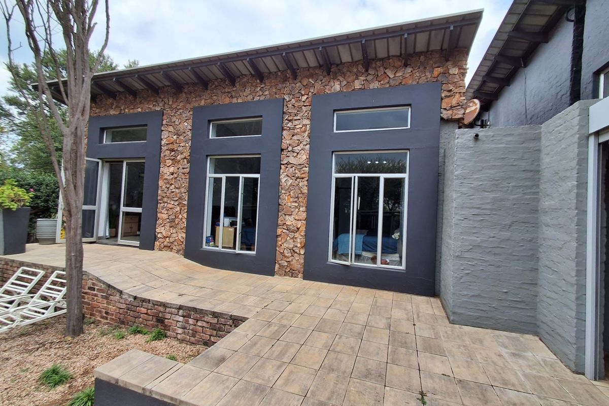 Rear exterior view of the property featuring stone cladding, modern dark-framed windows, and a paved patio area leading to the garden.