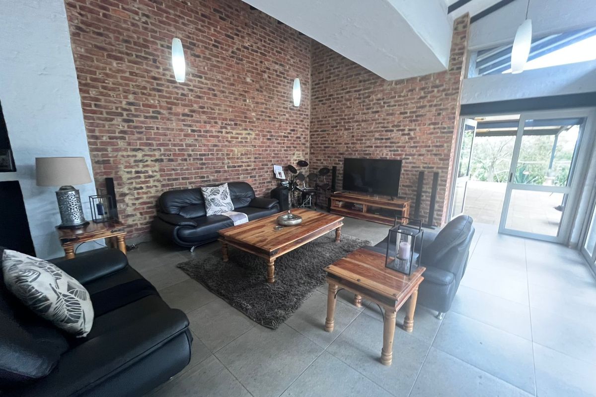 Spacious living room featuring a double-volume ceiling, exposed brick feature walls, large format floor tiles, and sliding glass doors leading to the patio.