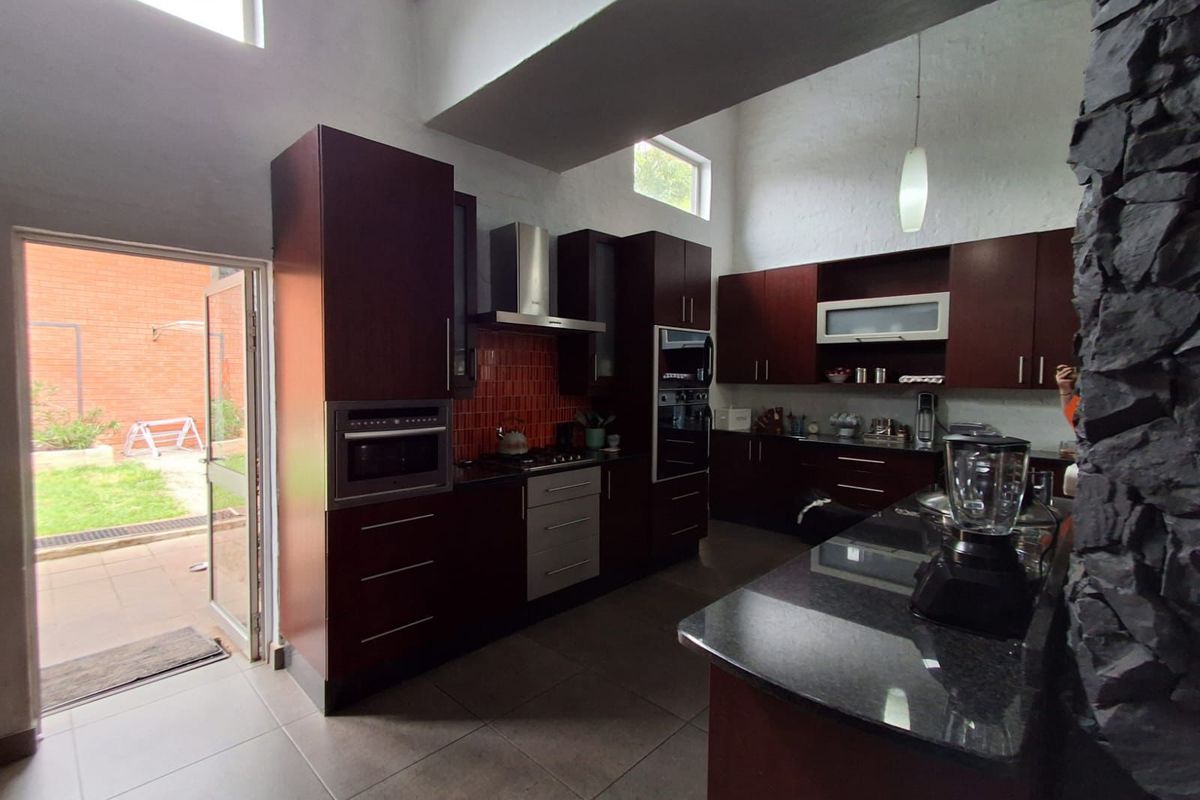 Modern kitchen featuring dark wood cabinetry, granite countertops, built-in oven, gas hob, extractor fan, and direct access to the rear patio area.
