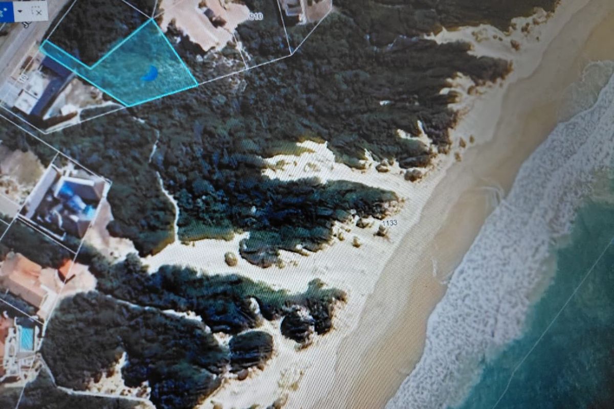 Aerial view of a vacant residential plot situated along the coastline, highlighting its proximity to the beach and surrounding natural landscape.