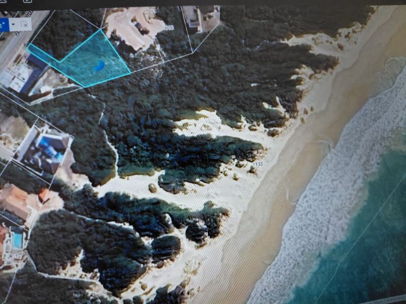 Aerial view of a vacant residential plot situated along the coastline, highlighting its proximity to the beach and surrounding natural landscape.