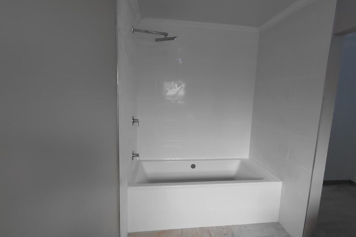 A clean, modern bathroom featuring a built-in bathtub with a wall-mounted shower head and white tiled surround.