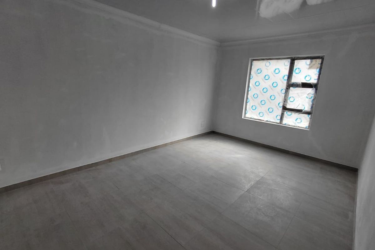 A clean, empty bedroom featuring neutral tiled flooring and a window with protective film still attached, ready for final finishing touches.