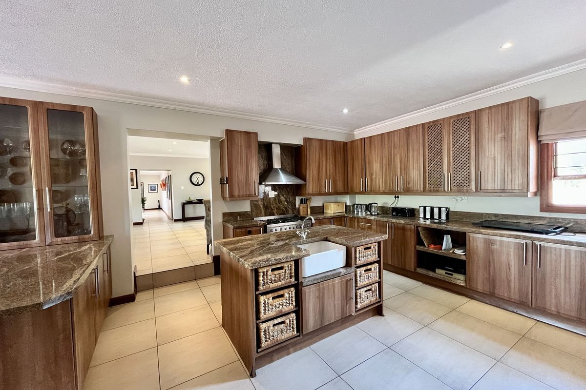 Spacious kitchen featuring wood-finish cabinetry, granite countertops, a central island with a farmhouse sink, and a stainless steel extractor fan.