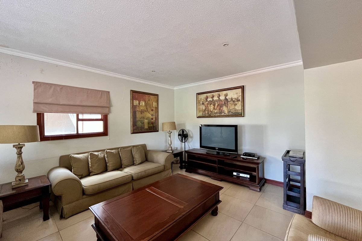 A comfortable living room featuring neutral tiled flooring, recessed ceiling lighting, and a window with a fitted roman blind.