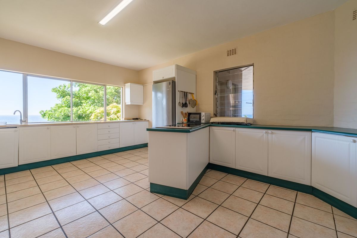 A functional kitchen featuring white cabinetry with green trim, tiled flooring, and large windows providing natural light and scenic views.