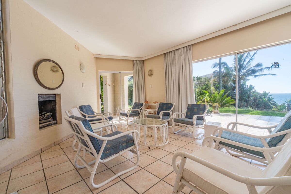 A sunlit living room featuring tiled flooring, a built-in fireplace, and large sliding glass doors that open to a patio with garden and ocean views.