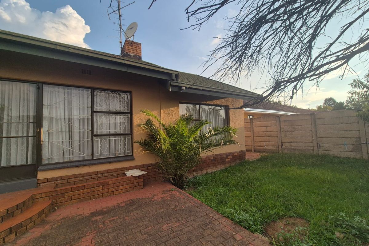 Rear view of the house featuring a brick paved patio area, garden space, and perimeter walling.
