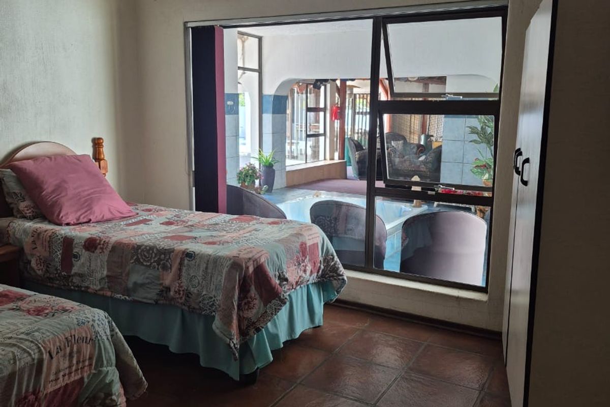 A bedroom featuring terracotta floor tiles and a large window providing a view into the adjacent covered patio area.