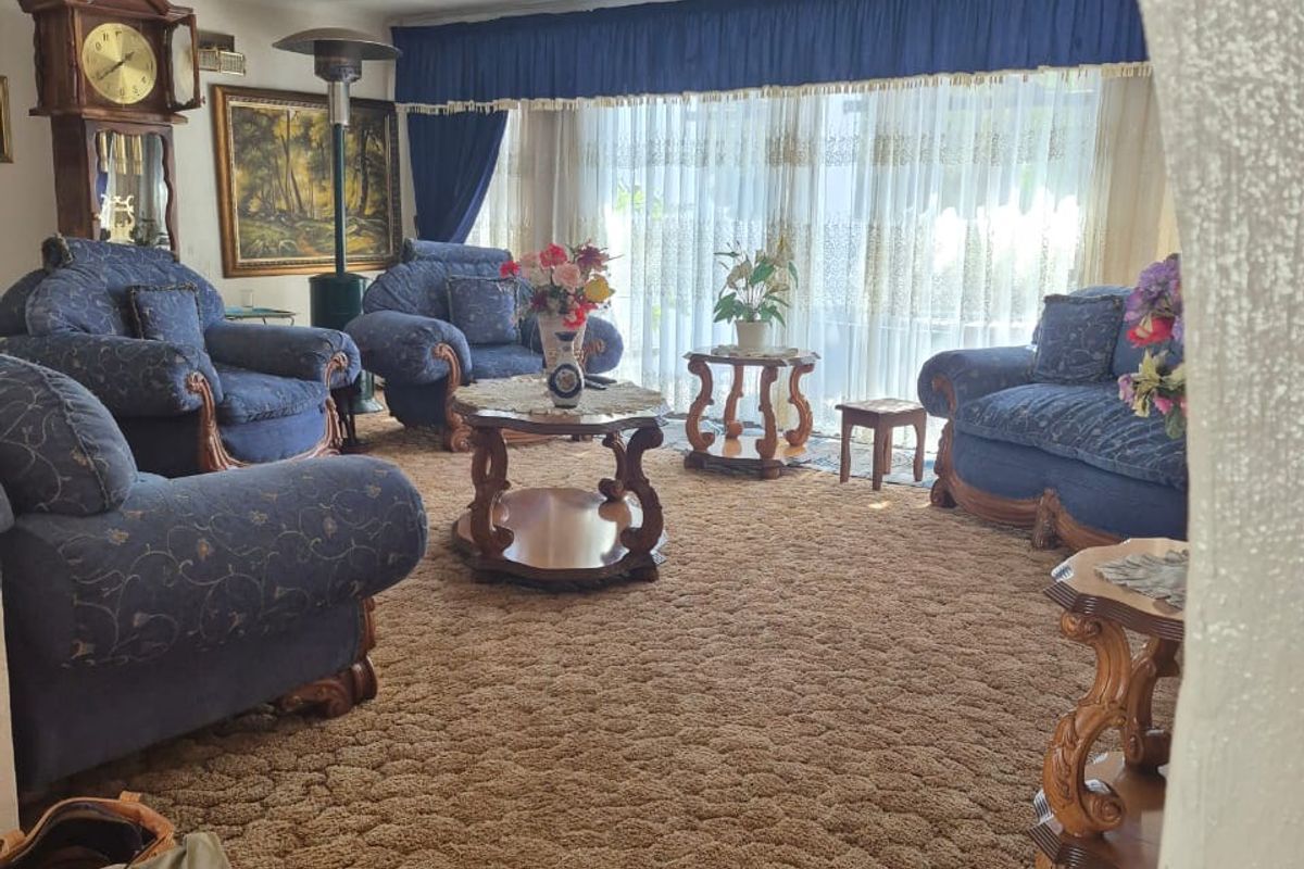 A traditional living room featuring wall-to-wall carpeting, large windows with drapery, and a central ceiling light fixture.