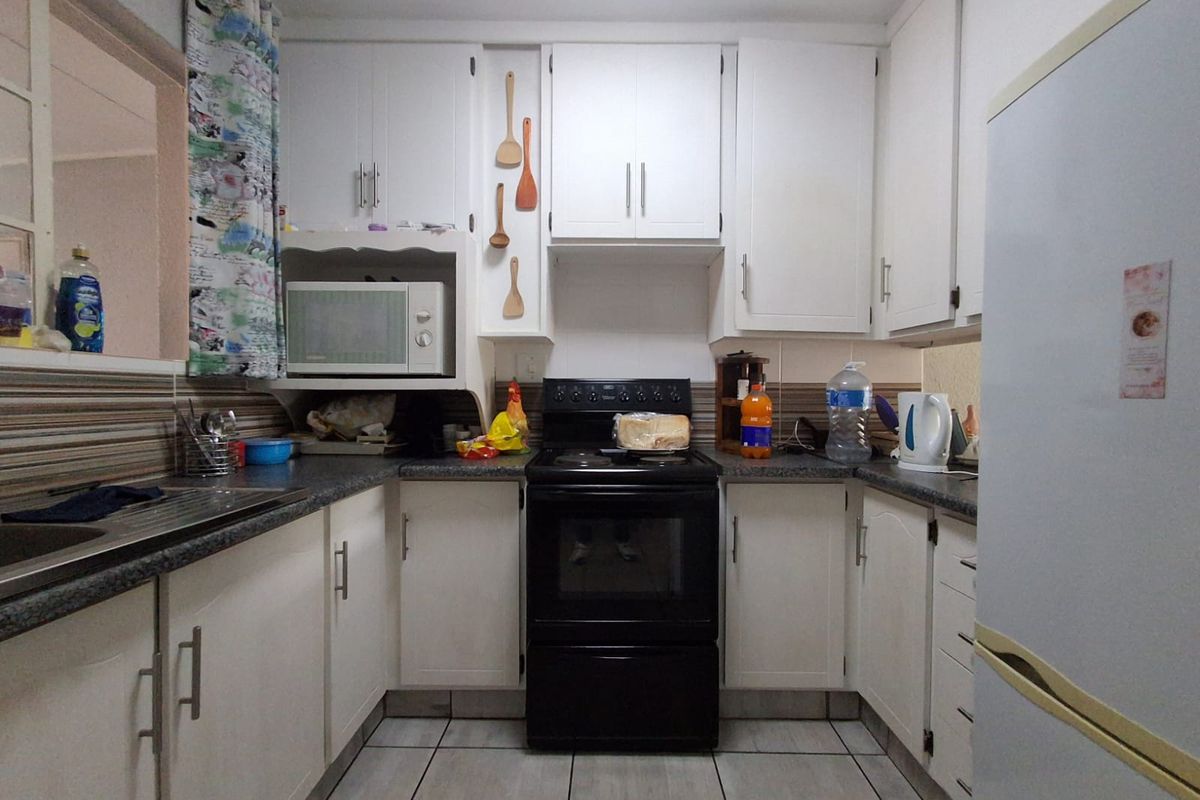 A functional kitchen featuring white cabinetry, dark laminate countertops, tiled flooring, and a built-in black oven and stove unit.