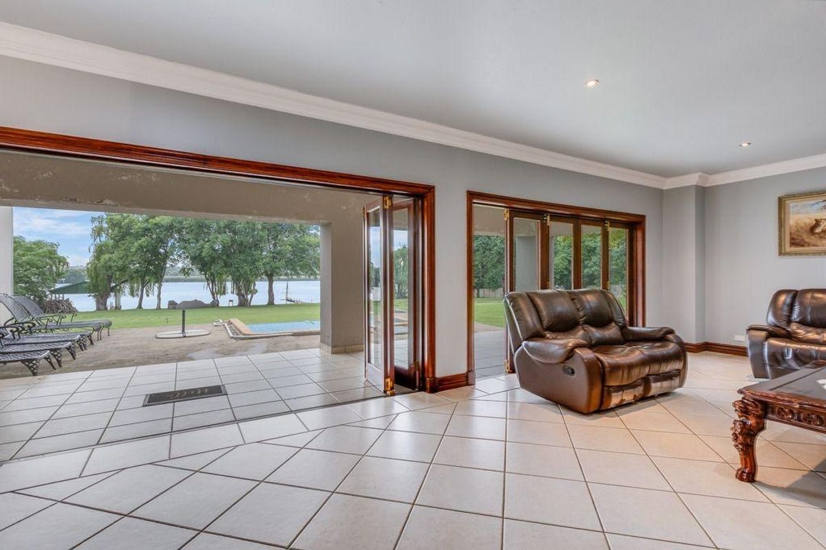 Spacious living area featuring large wooden bi-fold doors that open onto a covered patio with views of the garden and pool.