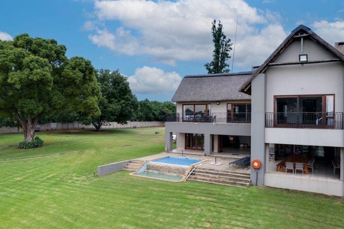 Spacious rear elevation featuring a thatched roof, covered patio, swimming pool, and expansive landscaped garden with mature trees.