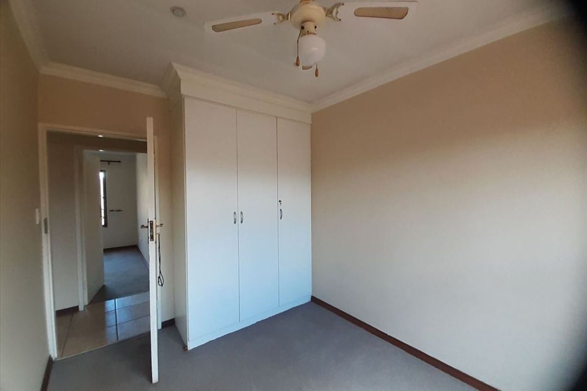 A bedroom featuring built-in cupboards, a ceiling fan, and neutral wall finishes, providing a functional and well-lit living space.