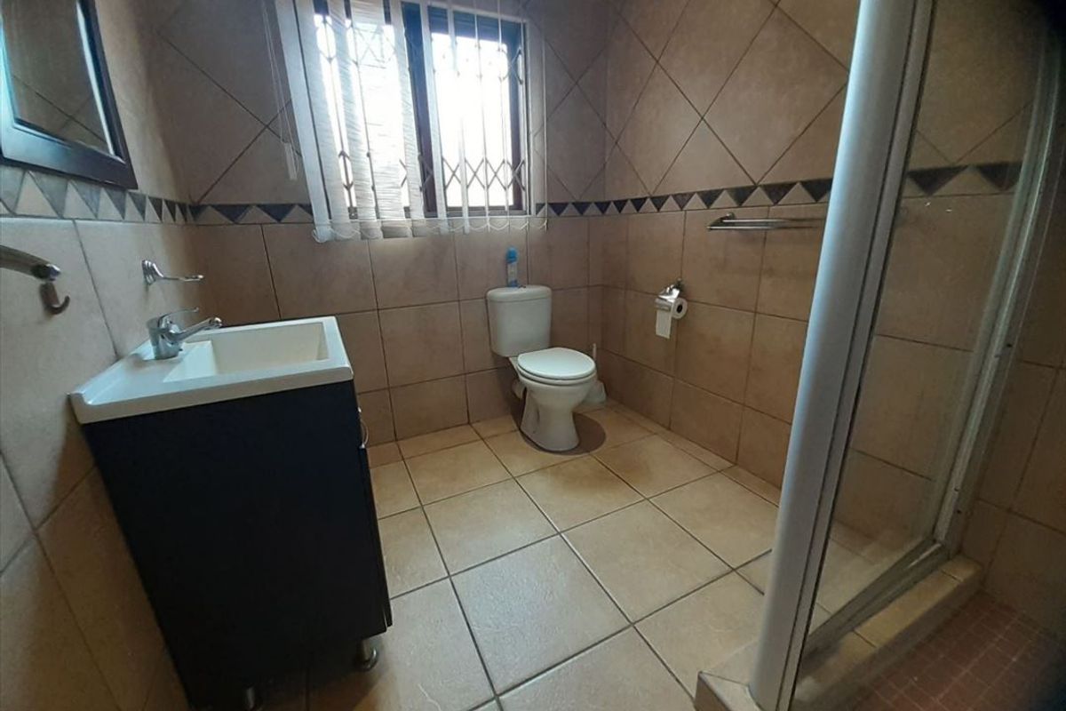 A functional bathroom featuring a shower enclosure, vanity basin, and toilet with neutral wall and floor tiling.