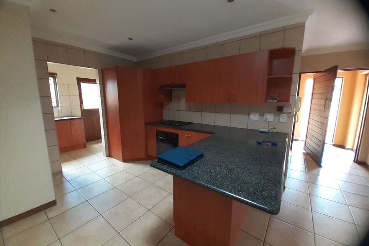 A functional kitchen featuring granite countertops, wooden cabinetry, a built-in oven and hob, and an adjacent scullery area with tiled flooring.