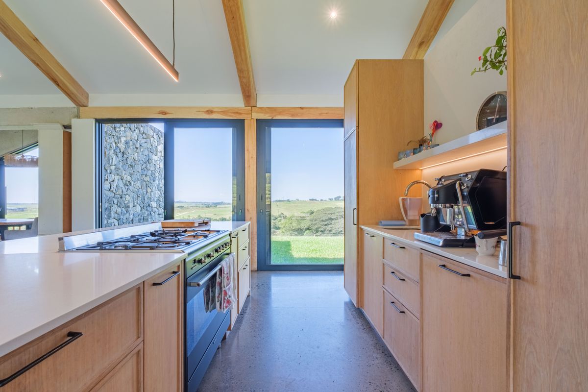 Modern kitchen featuring light wood cabinetry, stone countertops, a built-in gas range, and expansive glass doors opening to scenic rural views.