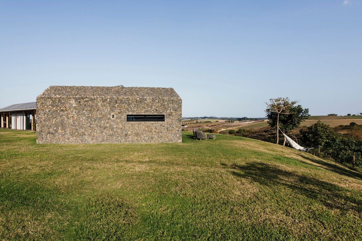 A view of the rear exterior of a stone-clad house set in a rural landscape with expansive green lawns.