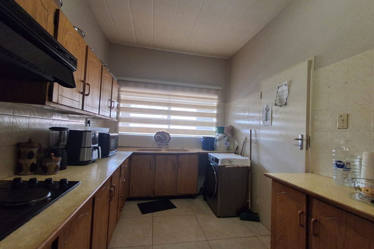 A functional kitchen featuring wooden cabinetry, integrated hob, extractor fan, and tiled flooring with a dedicated space for laundry appliances.