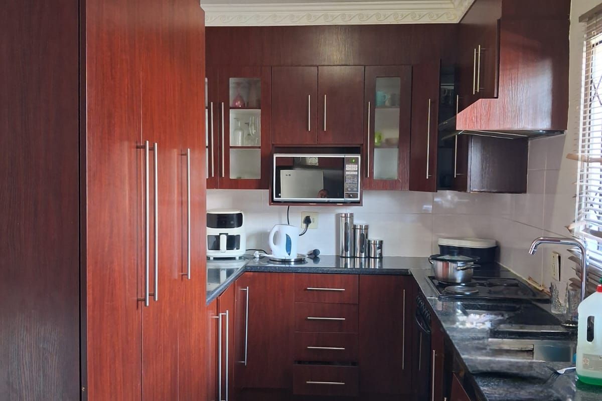 A functional kitchen featuring dark wood-toned cabinetry, granite countertops, a built-in microwave, and tiled flooring.