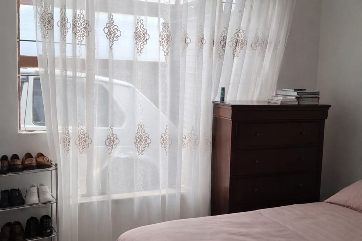 A bedroom featuring a large window with sheer curtains, neutral carpeting, and standard wall finishes.