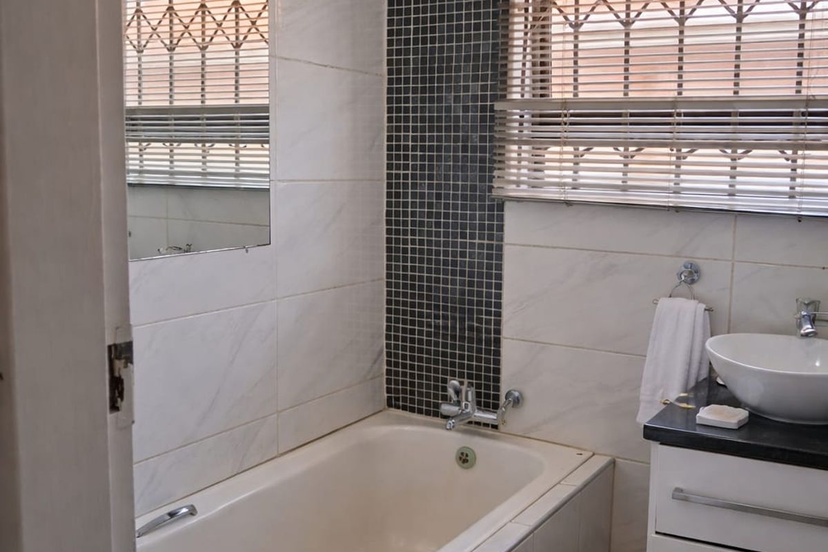 A compact bathroom featuring a built-in bathtub with mosaic tile accent, a modern vanity with vessel sink, and security bars on the window.