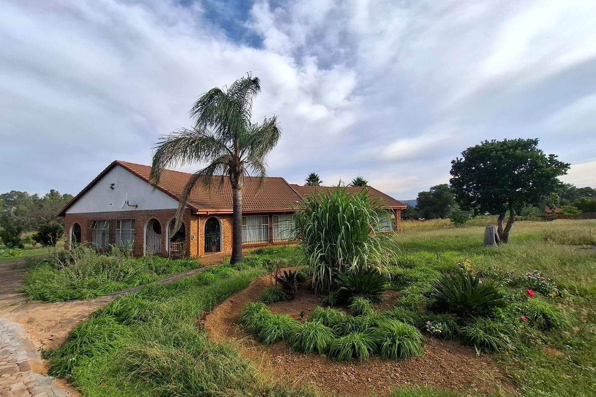 Rear view of a brick-built small holding residence featuring arched patio openings, a tiled roof, and an expansive, established garden area.