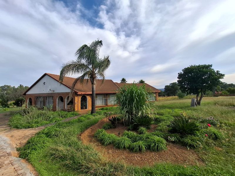 Rear view of a brick-built small holding residence featuring arched patio openings, a tiled roof, and an expansive, established garden area.