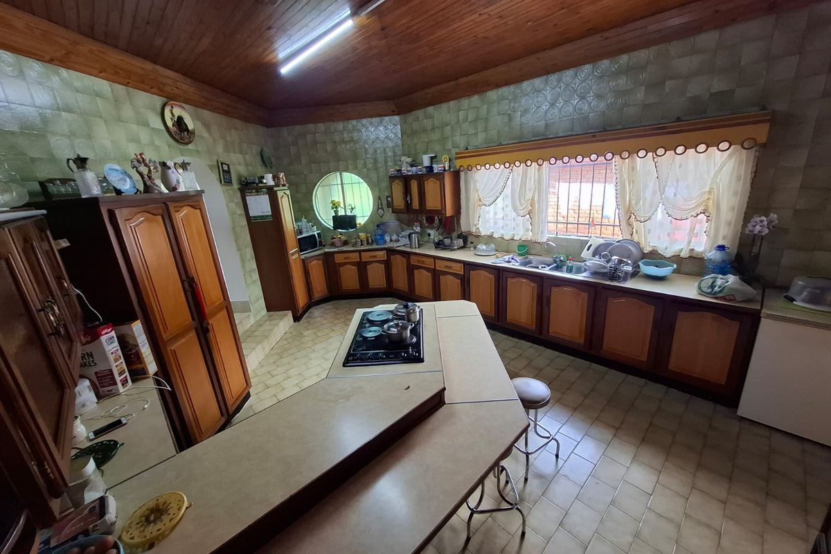 Spacious kitchen featuring extensive wooden cabinetry, a central island with a built-in gas hob, double sink, and a distinctive timber ceiling.