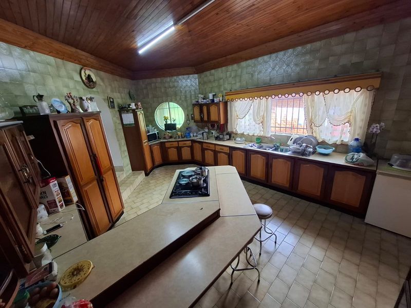 Spacious kitchen featuring extensive wooden cabinetry, a central island with a built-in gas hob, double sink, and a distinctive timber ceiling.