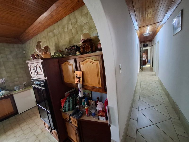 A kitchen area featuring built-in wooden cabinetry, a built-in oven, and tiled flooring, leading into a hallway with a timber ceiling.