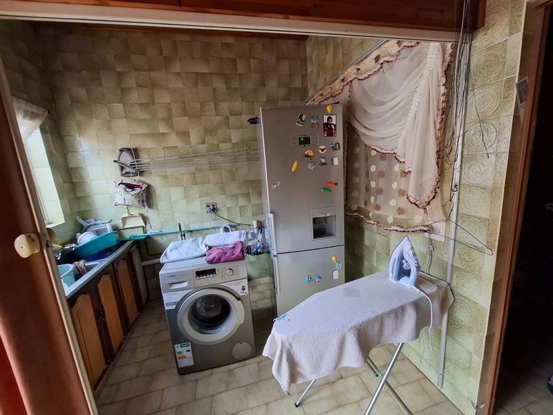 A functional laundry area featuring tiled walls, a built-in sink, and dedicated plumbing connections for laundry appliances.