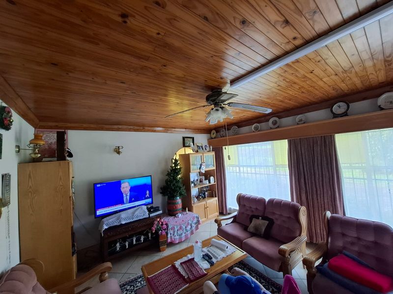 A living room featuring a warm timber-paneled ceiling, ceiling fan, tiled floors, and large sliding doors providing natural light.