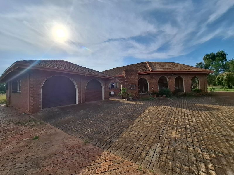 Front elevation of a brick-built small holding featuring a double garage, arched architectural details, and an extensive paved driveway area.