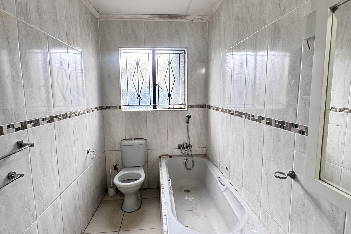 A compact bathroom featuring floor-to-ceiling wall tiles, a built-in bathtub, a standard toilet, and a wall-mounted basin.