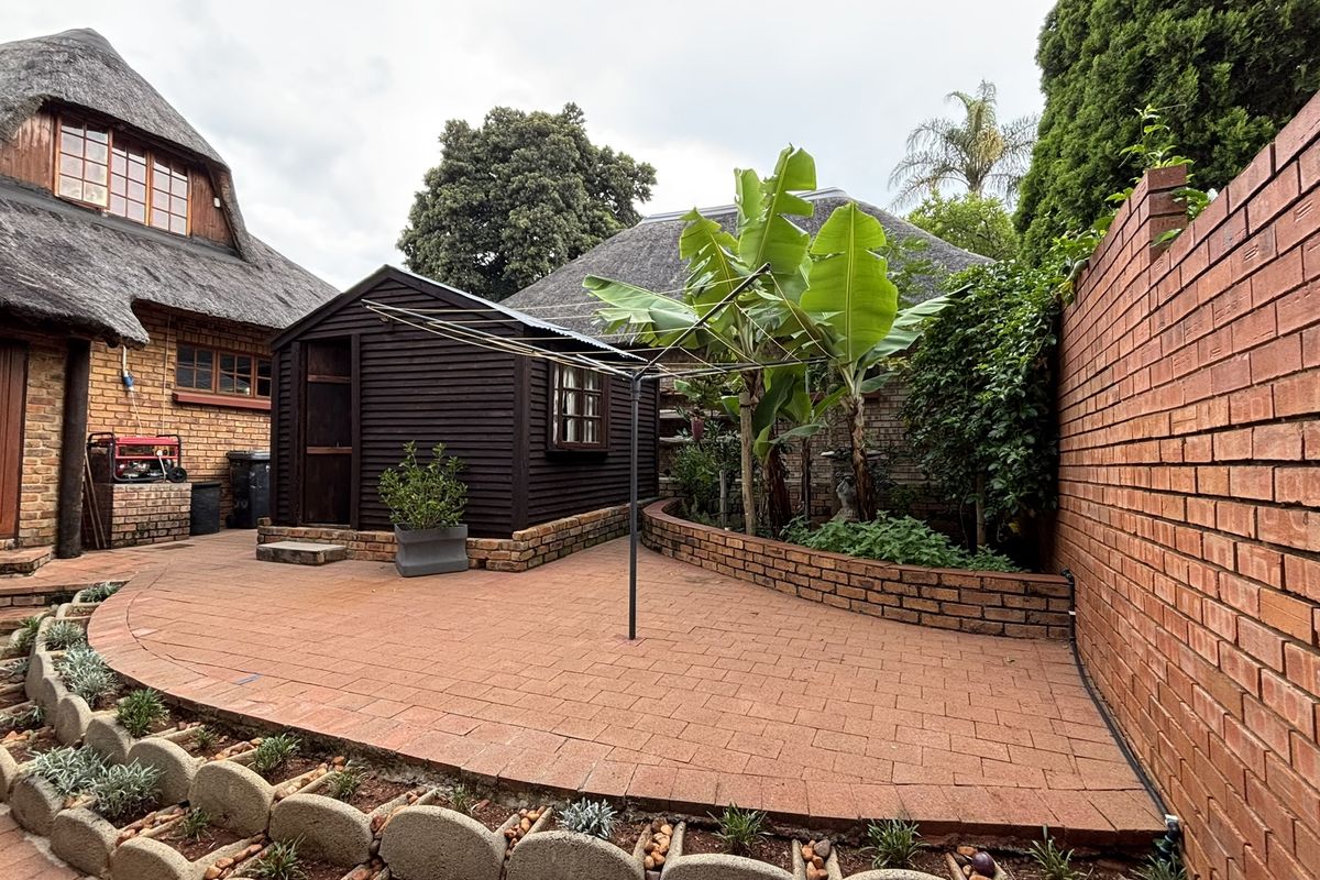 A rear courtyard featuring paved flooring, a detached timber outbuilding, and a high brick boundary wall, providing a private outdoor space.