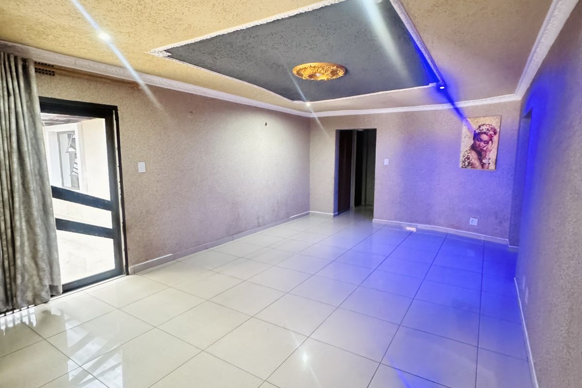 A spacious, empty living area featuring large format floor tiles, a decorative recessed ceiling with integrated lighting, and access to an outdoor space.