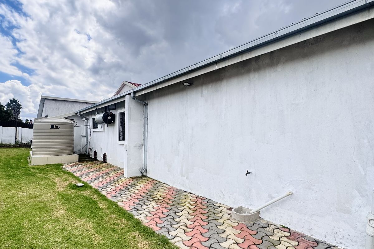 Rear exterior view of the property featuring a paved walkway, a water storage tank, and a grass lawn area.