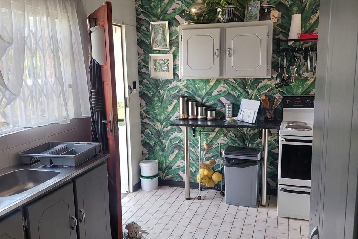 A compact kitchen featuring grey cabinetry, a freestanding stove, tiled flooring, and a distinctive botanical wallpaper feature wall.