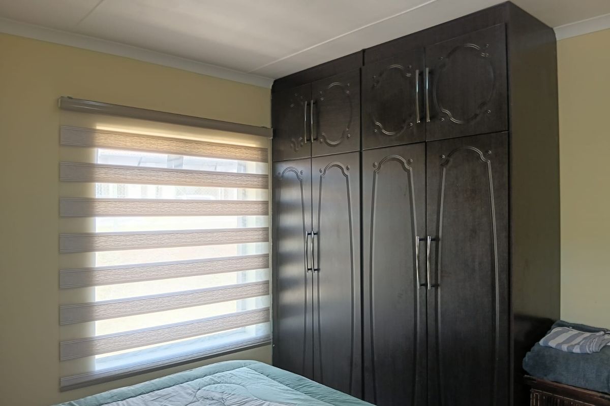 A bedroom featuring dark wood built-in cupboards and a modern zebra-style roller blind on the window.