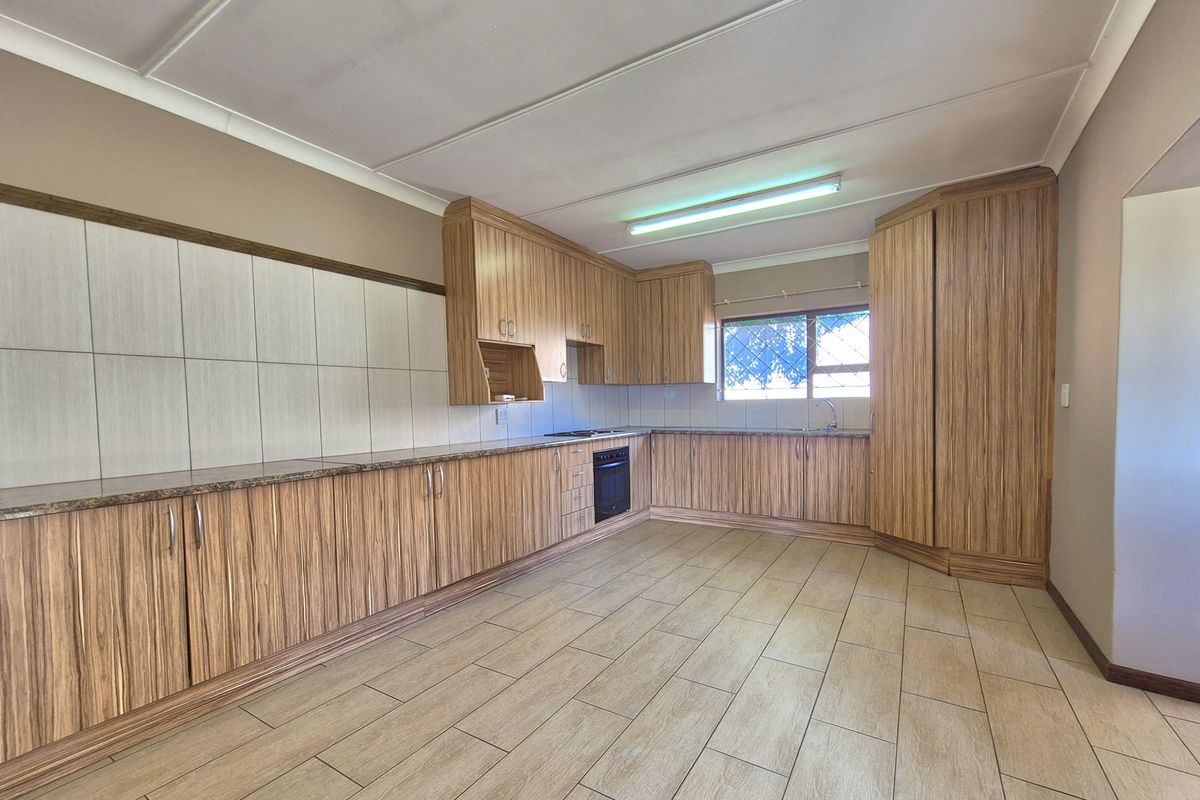 A spacious kitchen featuring wood-grain cabinetry, granite countertops, a built-in oven and hob, and tiled flooring.
