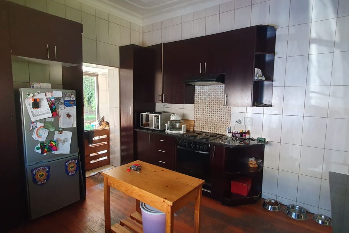 A functional kitchen featuring dark wood cabinetry, built-in oven and hob, tiled splashbacks, and direct access to the rear exterior.