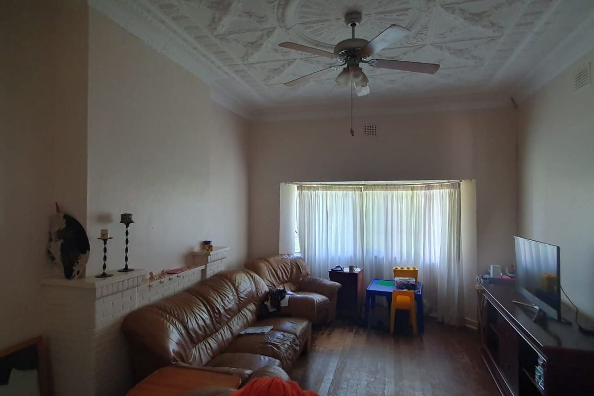 Spacious living room featuring ornate period ceiling detailing, a brick fireplace surround, and a large bay window allowing for natural light.