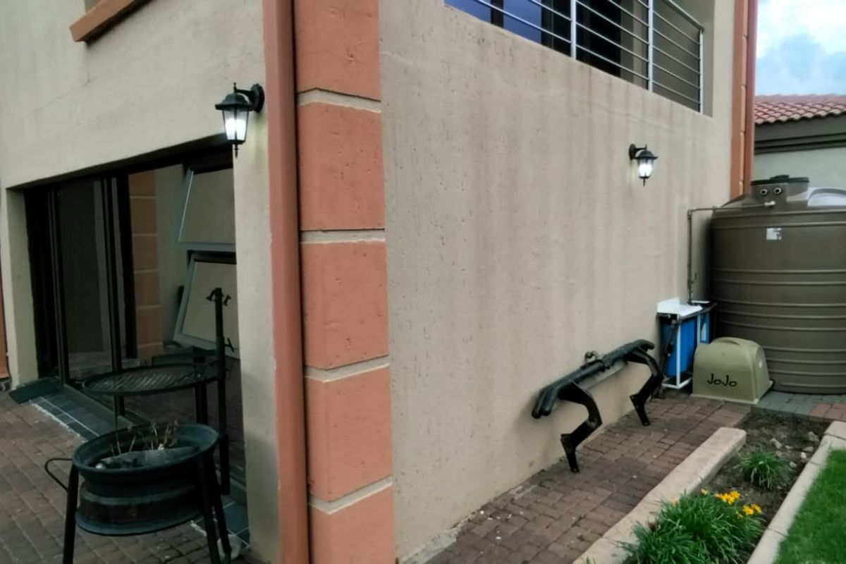Rear exterior view of the property featuring a paved patio area, wall-mounted lighting, and a large water storage tank.