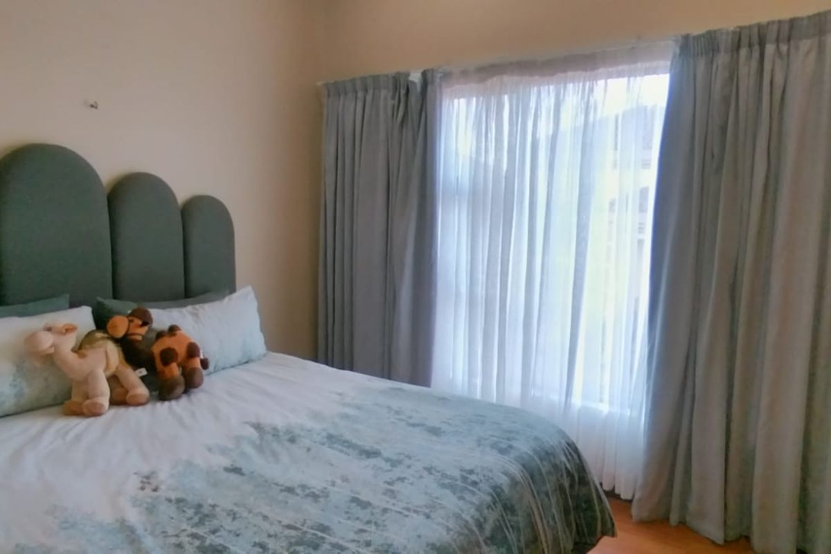 A comfortable bedroom featuring a large window with floor-to-ceiling curtains and a built-in headboard.