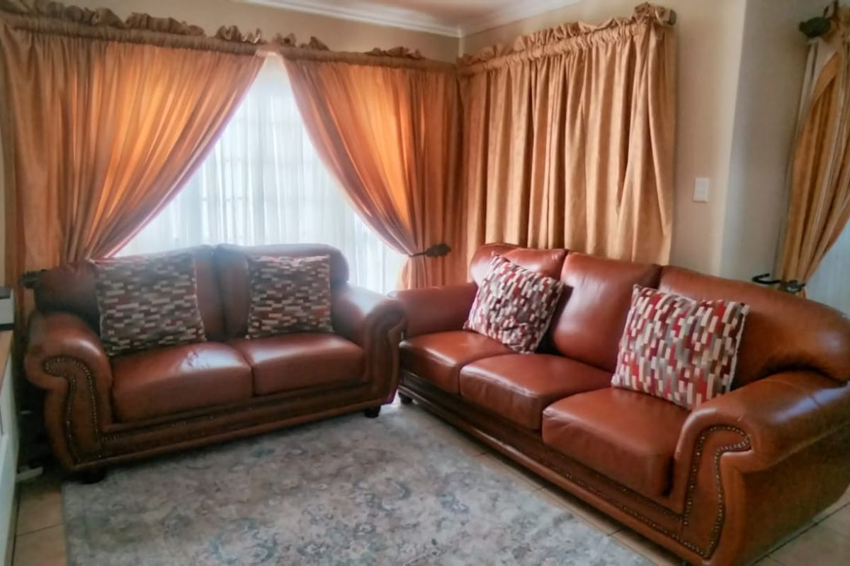 A comfortable living room area featuring tiled flooring and large windows dressed with curtains, providing a warm and inviting space for relaxation.