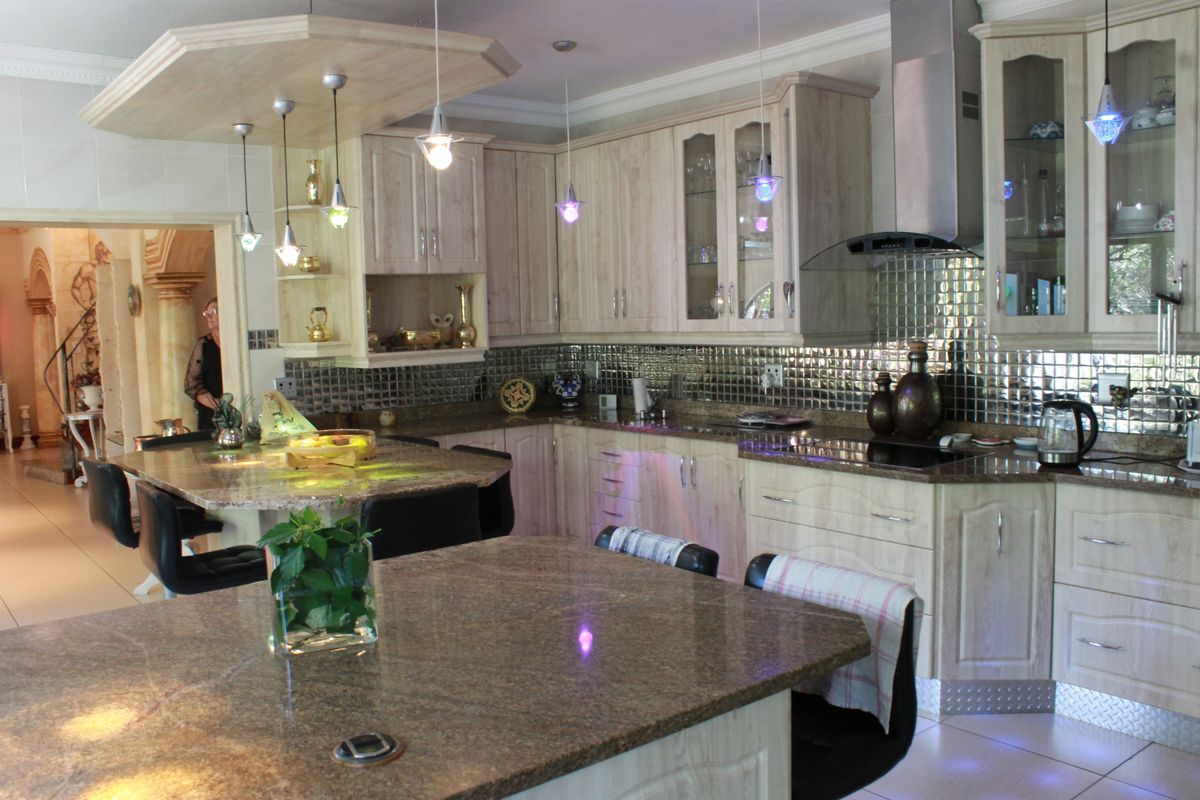 Spacious kitchen featuring granite countertops, extensive built-in cabinetry, a central island, and a modern stainless steel extractor fan with a mosaic tile backsplash.