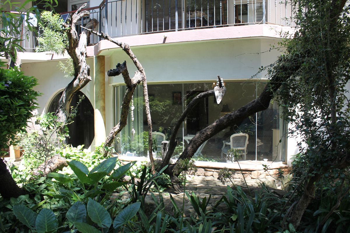Rear view of the property featuring a curved glass wall, stone patio area, and an upper-level balcony with wrought iron railings.