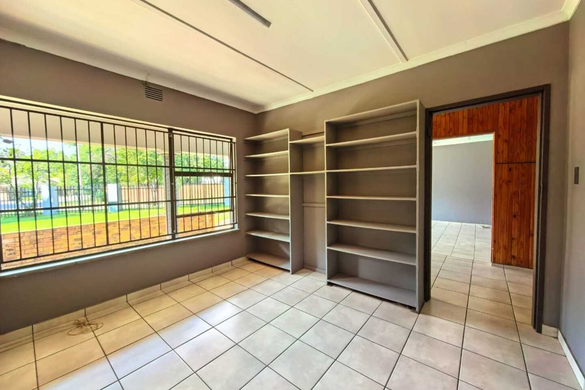 A functional room featuring tiled flooring, built-in shelving units, and large windows with security bars, offering a versatile space for an office or study.