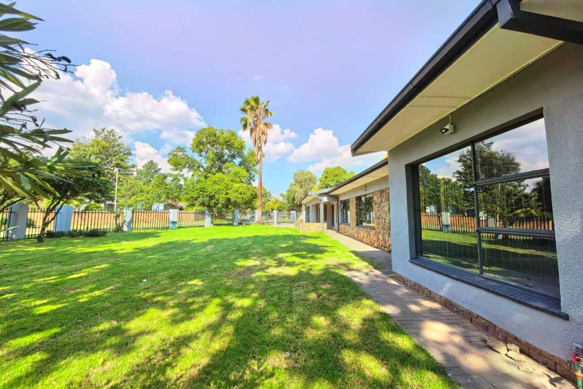 A spacious rear garden featuring a well-maintained lawn, paved walkway, and stone-clad exterior wall with large windows.